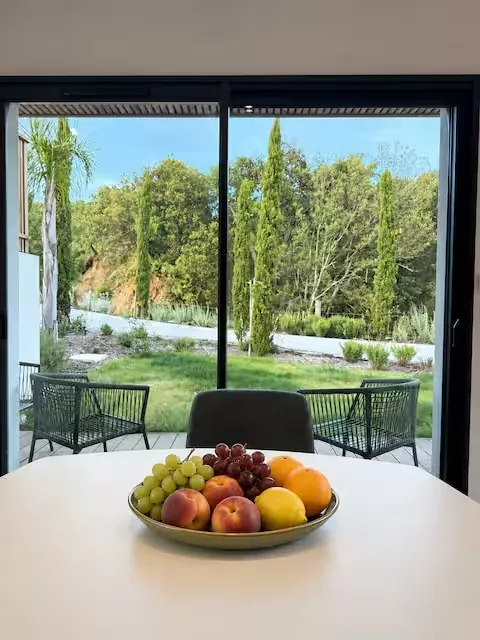 Table de salle à manger avec corbeille de fruits et vue sur le jardin – L’Annexe du Domaine de la Subérine