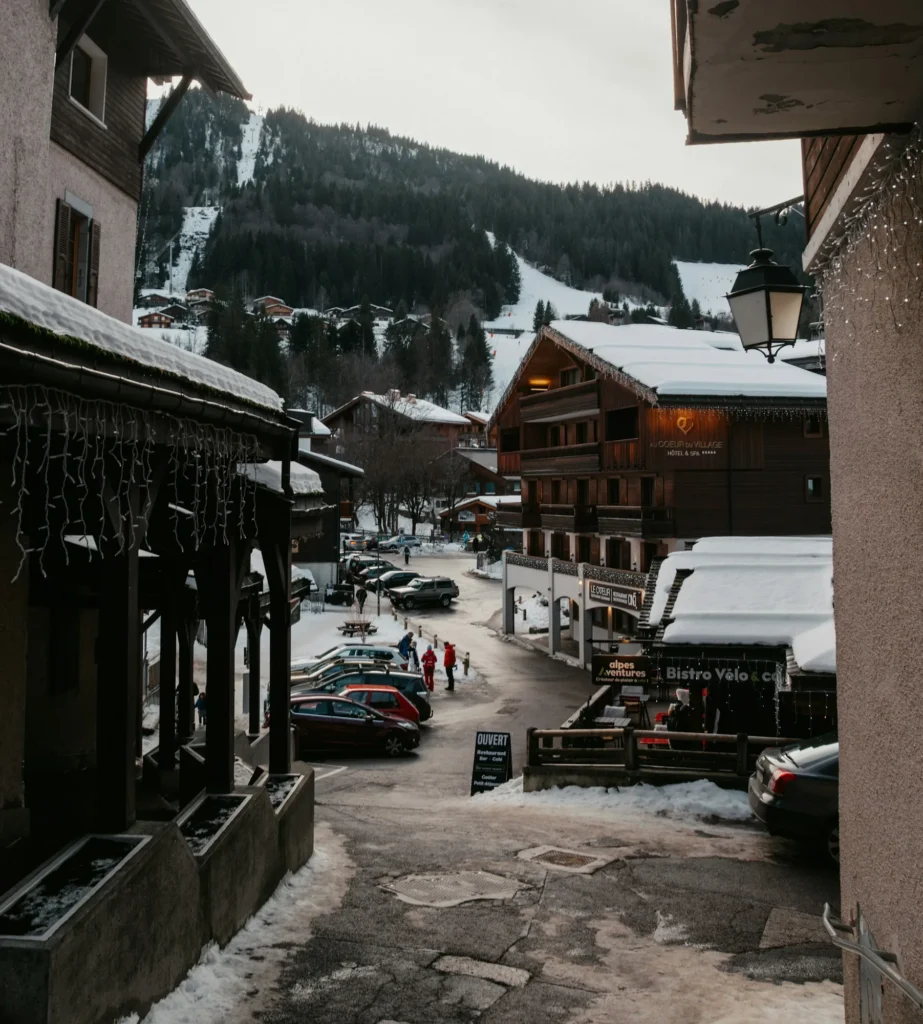 Rue du village du Grand-Bornand en hiver, chalets enneigés et pistes en arrière-plan
